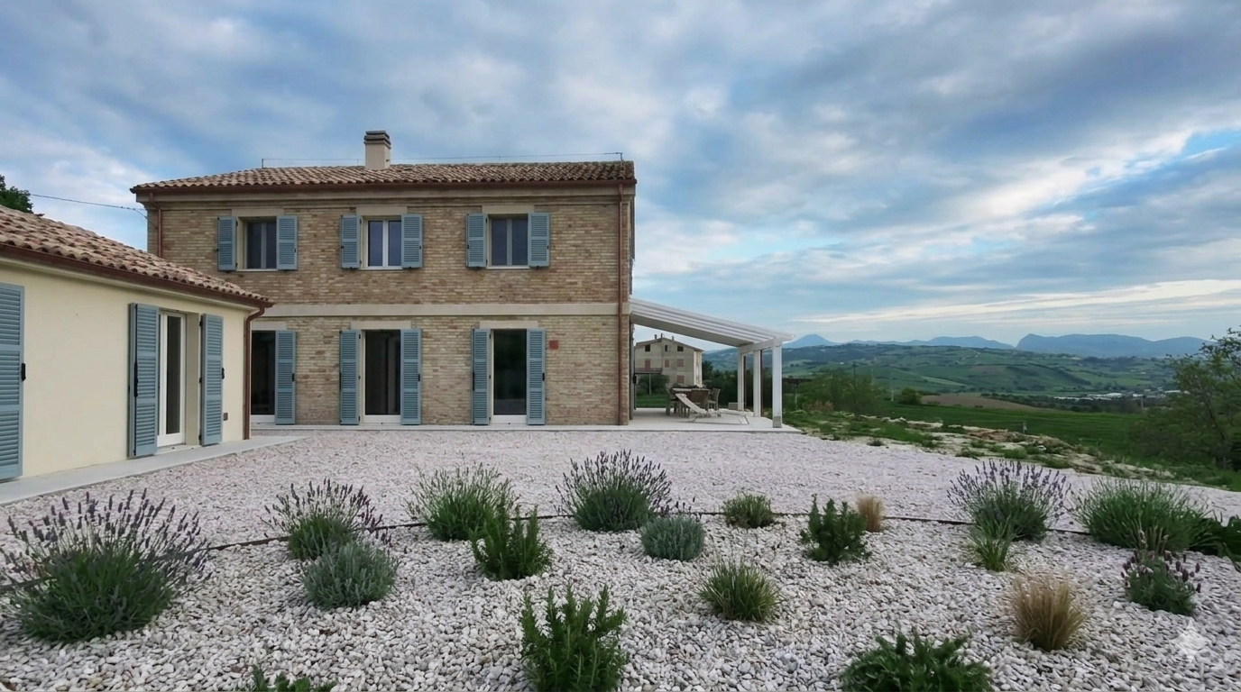Full façade of Villa Vetere with sage-green shutters above a gravel garden of lavender and the rolling Marche hills beyond